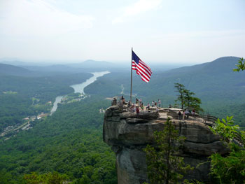 The American Flag waves proudly on top of Chimney Rock with scenic Lake Lure in the background.
